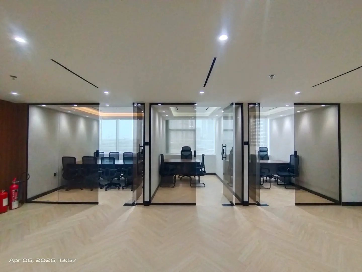 Modern office space with three glass-walled conference rooms, herringbone floors, and city views.