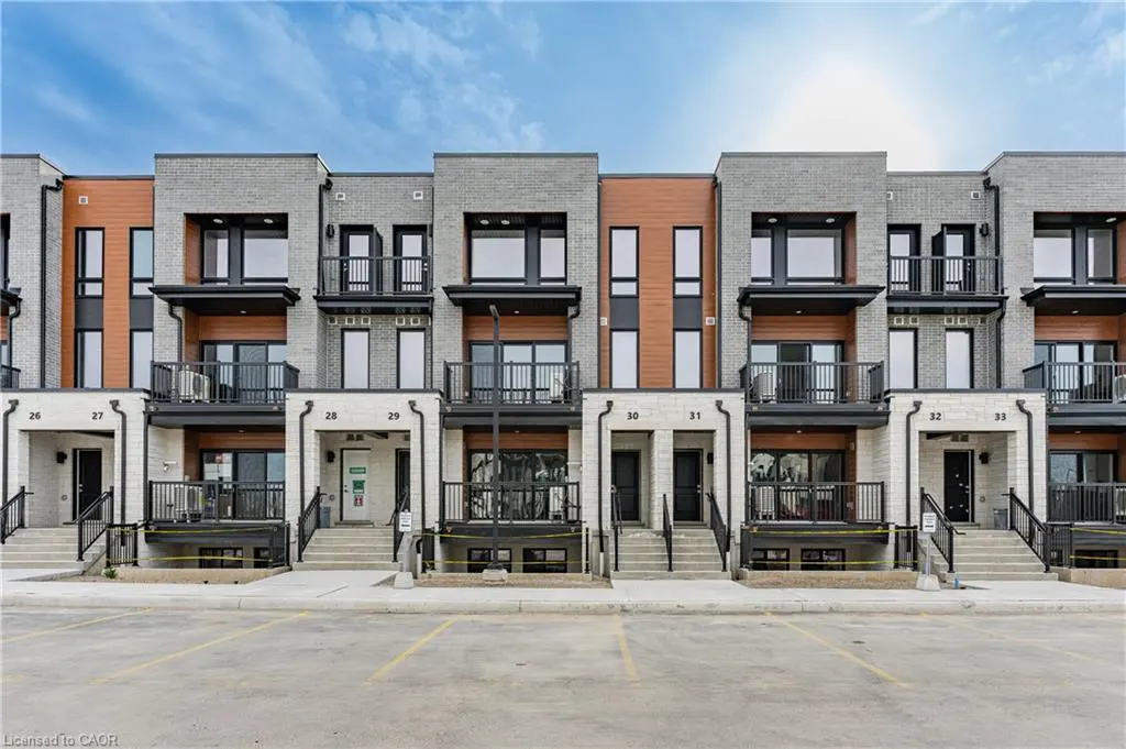 Row of modern townhouses with gray brick and wood accents, black balconies, and parking lot in front. Blue sky.