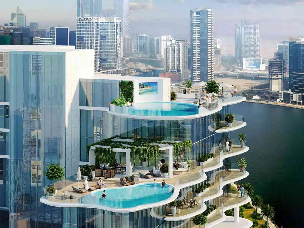 Exterior view of a modern high-rise building with pools, terraces, and greenery overlooking a cityscape and waterway.