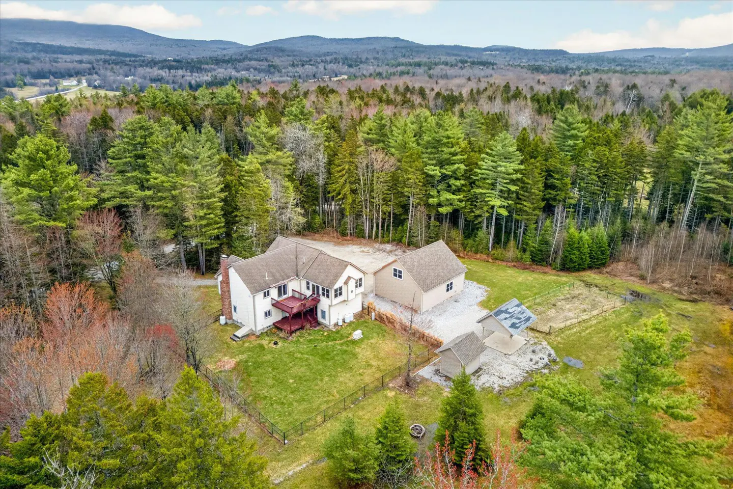 Aerial view of a white house with a red deck, surrounded by green trees and mountains in the background.