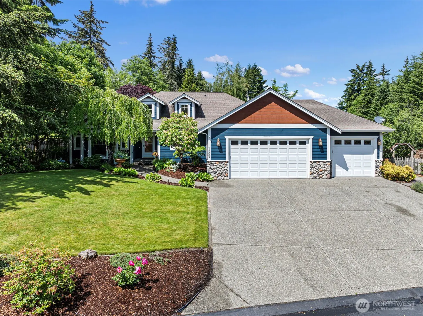 Two-story blue house with a brown roof, white garage doors, green lawn, and trees.