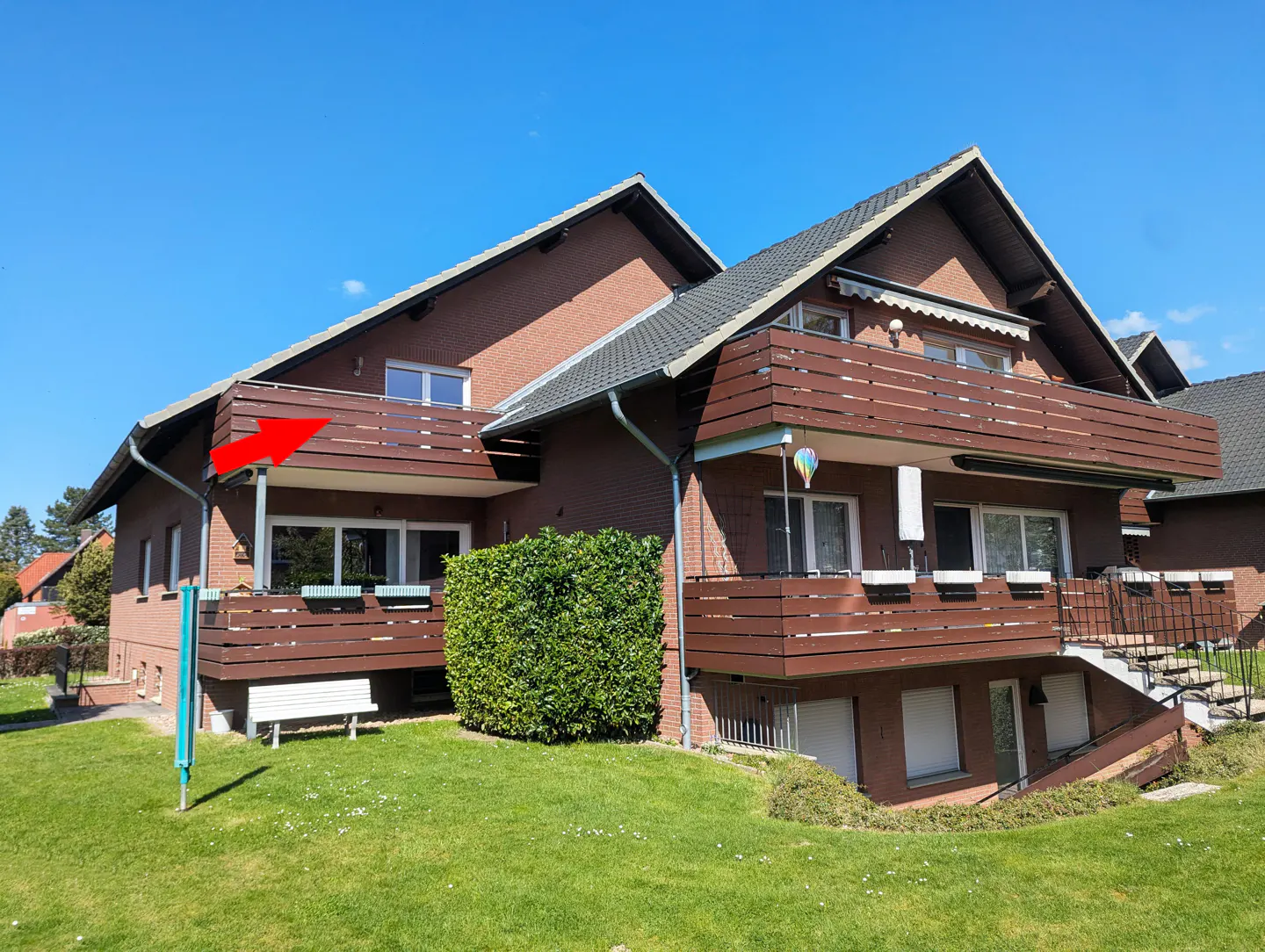 Exterior of a brick apartment building with brown balconies and a green lawn. An arrow points to the top balcony.