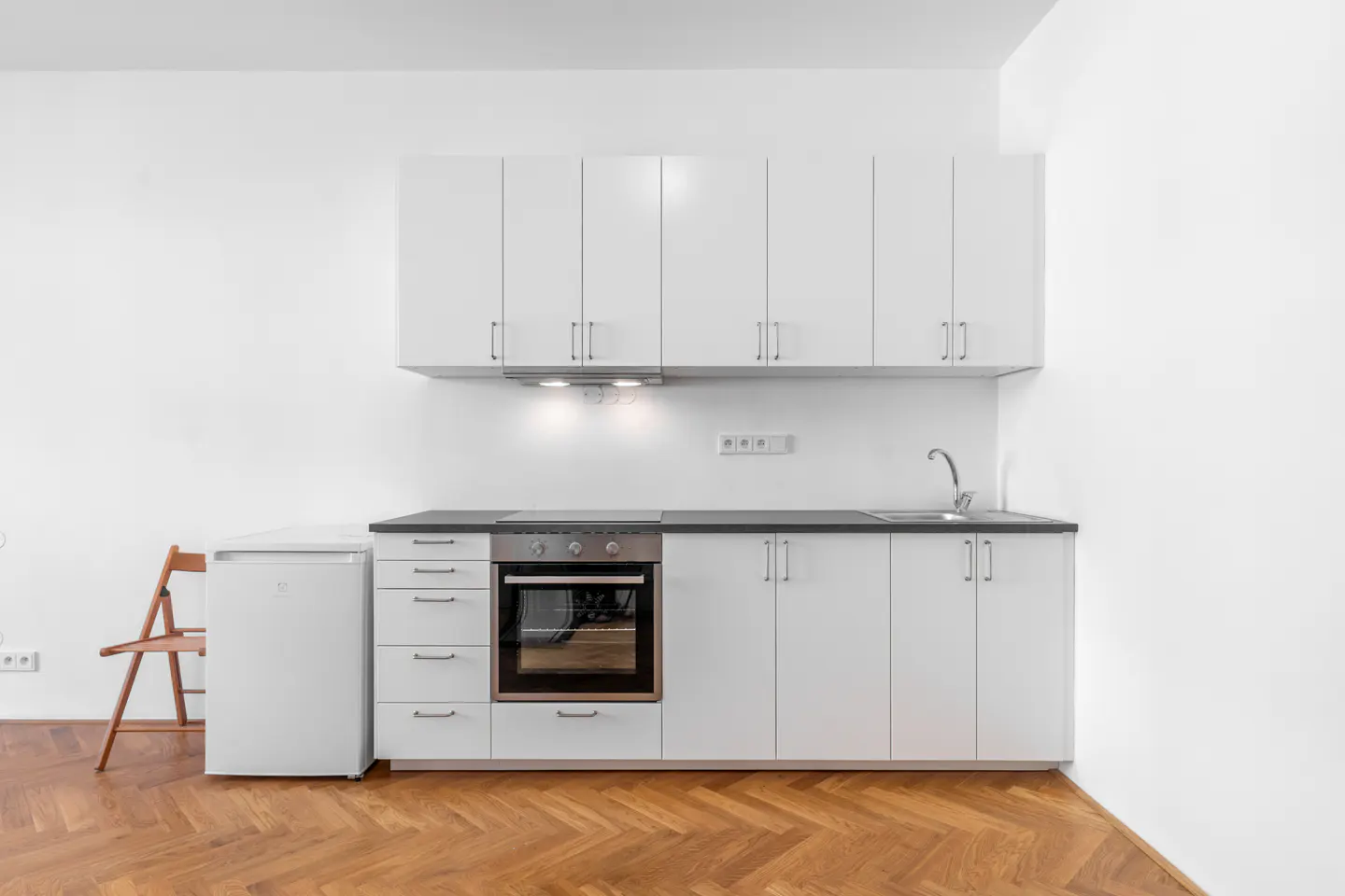 A bright, modern kitchen with white cabinets, dark countertops, and a wood floor.