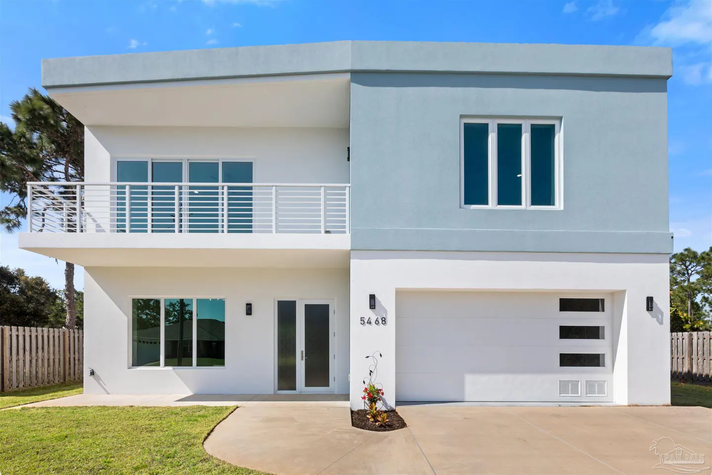 Two-story modern home with white and blue exterior, balcony, and white garage door. Lawn and blue sky in background.