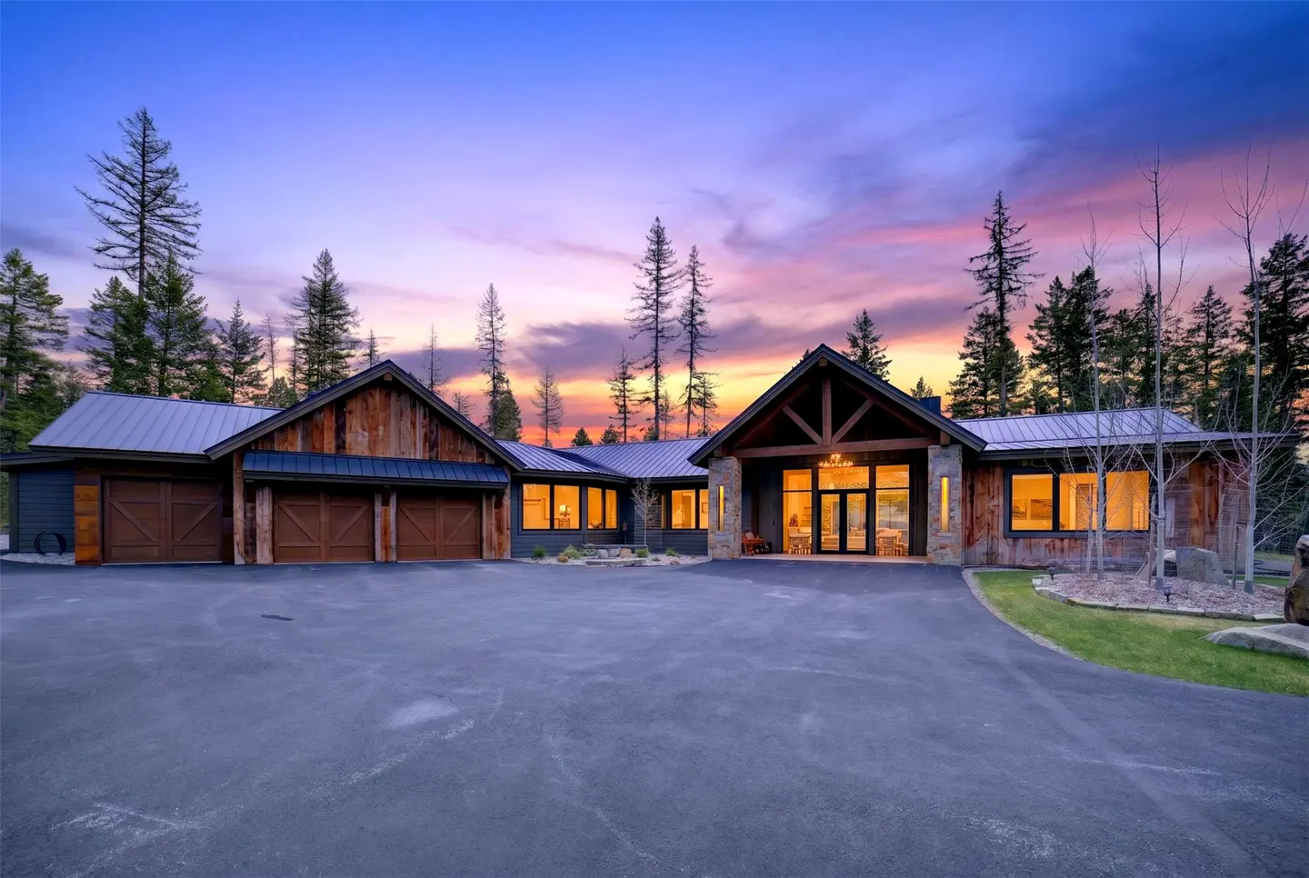 Exterior of a rustic home with a metal roof, wood siding, and a large driveway at sunset.