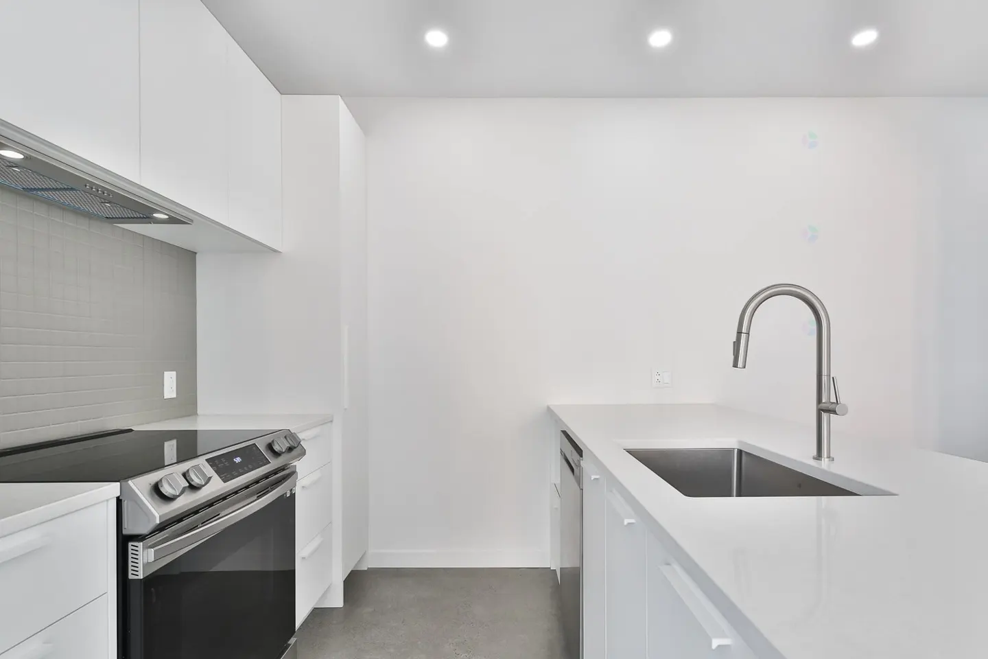 Bright, modern kitchen with white cabinets, stainless steel appliances, and a gray tile backsplash. A sink and faucet are on the right.