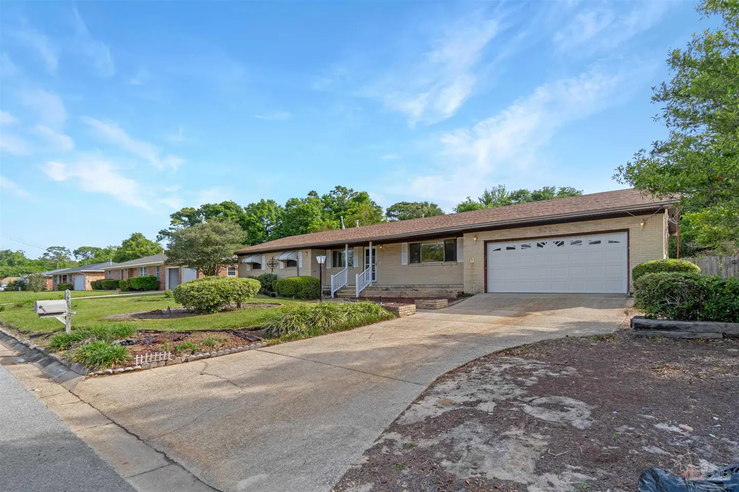 A single-story beige house with a white garage door and a brown roof on a sunny day.