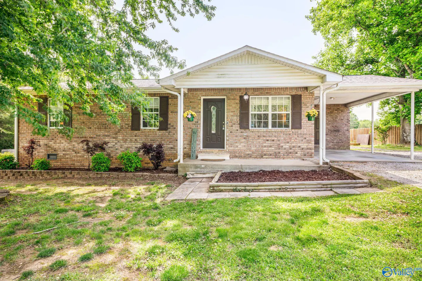 A single-story brick house with a carport, brown shutters, and a green lawn.