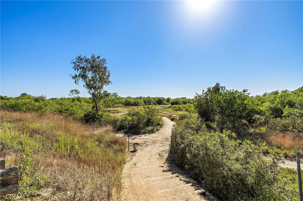 A dirt path winds through green and brown vegetation under a clear blue sky.