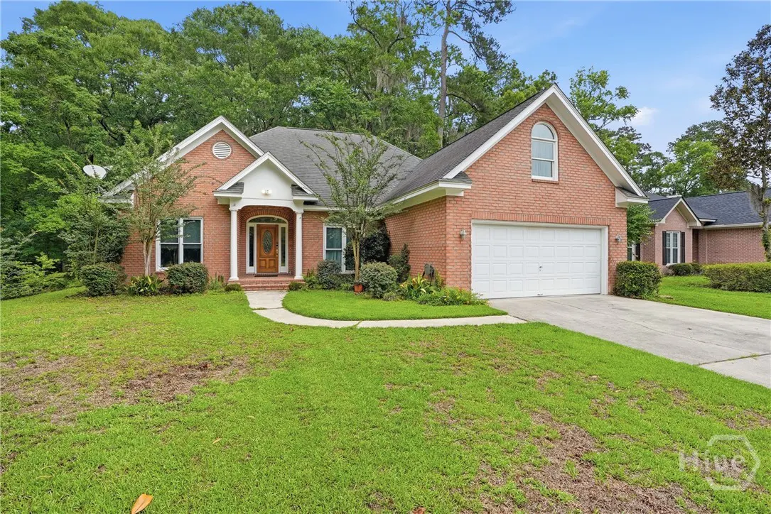 Single-story red brick house with a white garage, arched window, and a green lawn surrounded by mature trees.