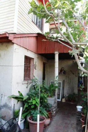 Exterior view of a house with a red roof, a barred window, and a covered porch with a white column. Potted plants line the walkway.