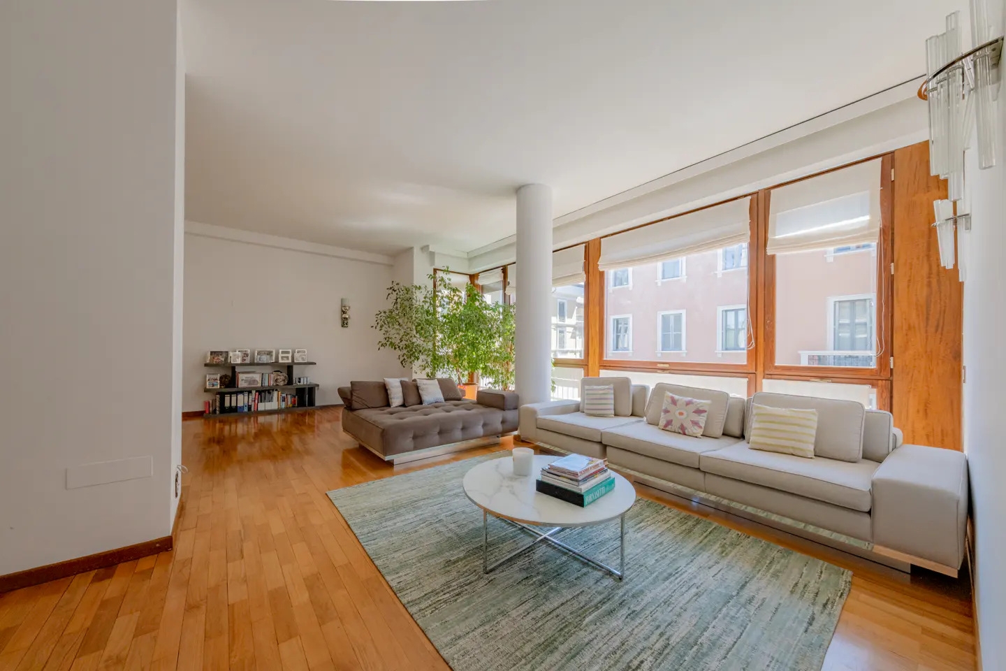 Bright living room with hardwood floors, a large window, and two sofas. A round marble table sits on a green rug.