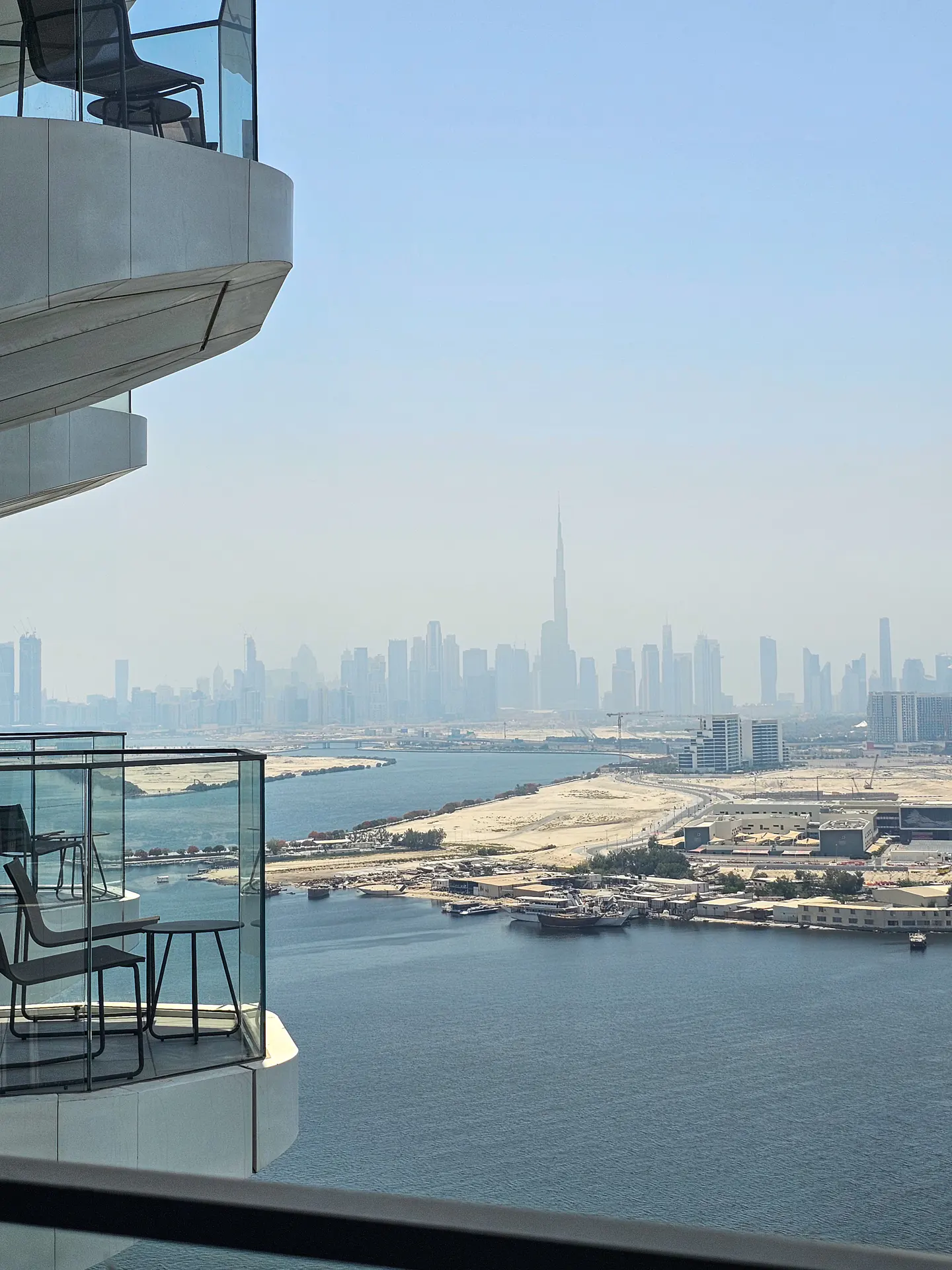 View from a balcony with chairs and a table overlooking the Dubai skyline and the water.