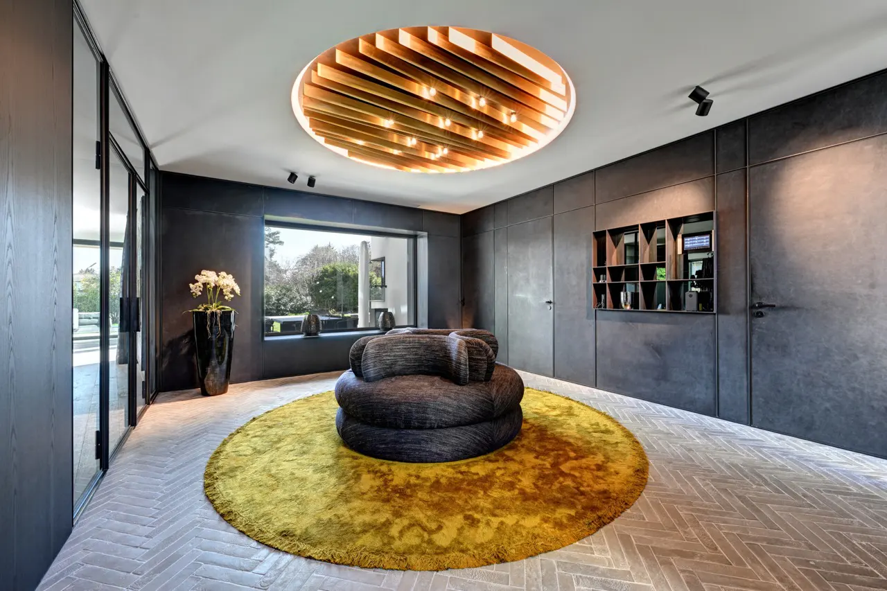 A modern living room with a round yellow rug, a gray sofa, and a wooden ceiling light.
