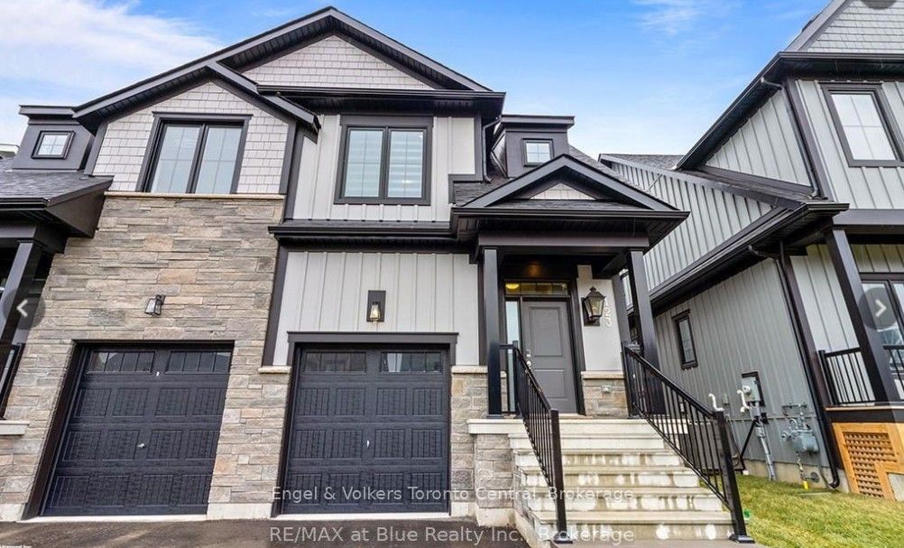 Two-story townhouse with gray stone and white siding, black trim, and a black garage door. Steps lead to a covered porch.