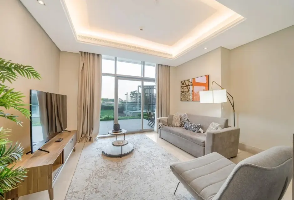 Living room with gray sofa, chaise lounge, TV, and balcony view. Neutral tones, modern decor, and natural light.