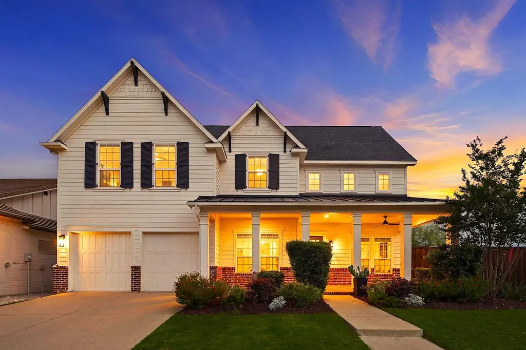Two-story white house with black shutters and a covered porch at dusk. The sky is blue and orange.