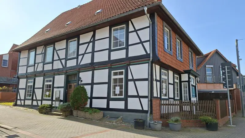 Two-story timber frame house with white walls and black beams, red tile roof, and a brick walkway.