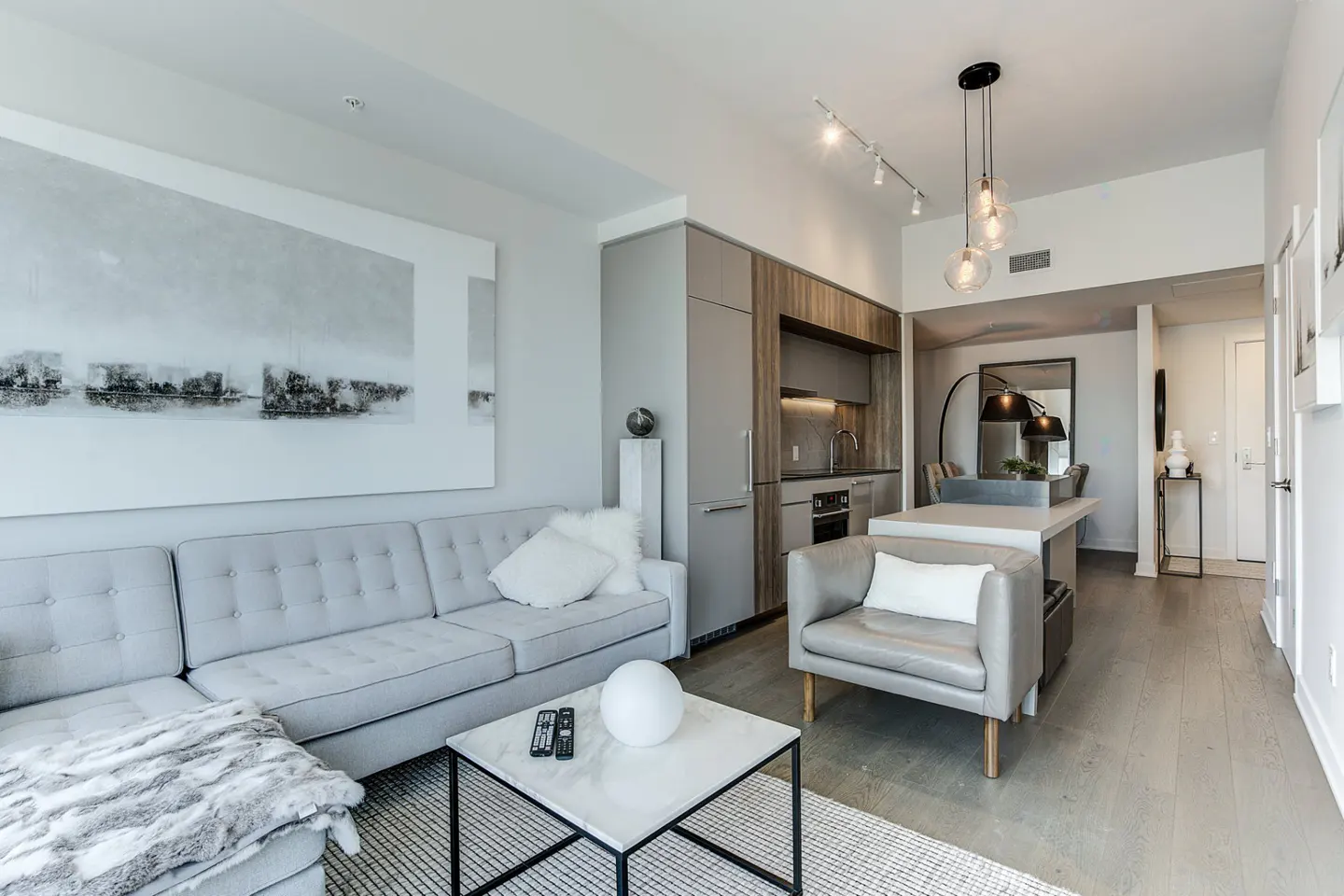 Bright, modern condo living room with gray sofa, marble coffee table, and open kitchen. Large abstract art on the wall.