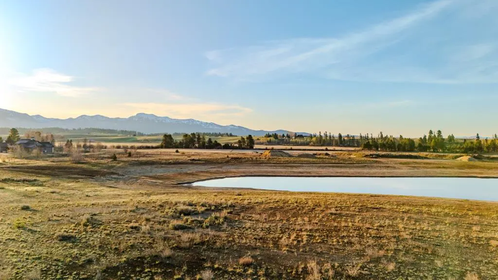 Scenic view of a pond surrounded by golden fields, with mountains and a blue sky in the background.