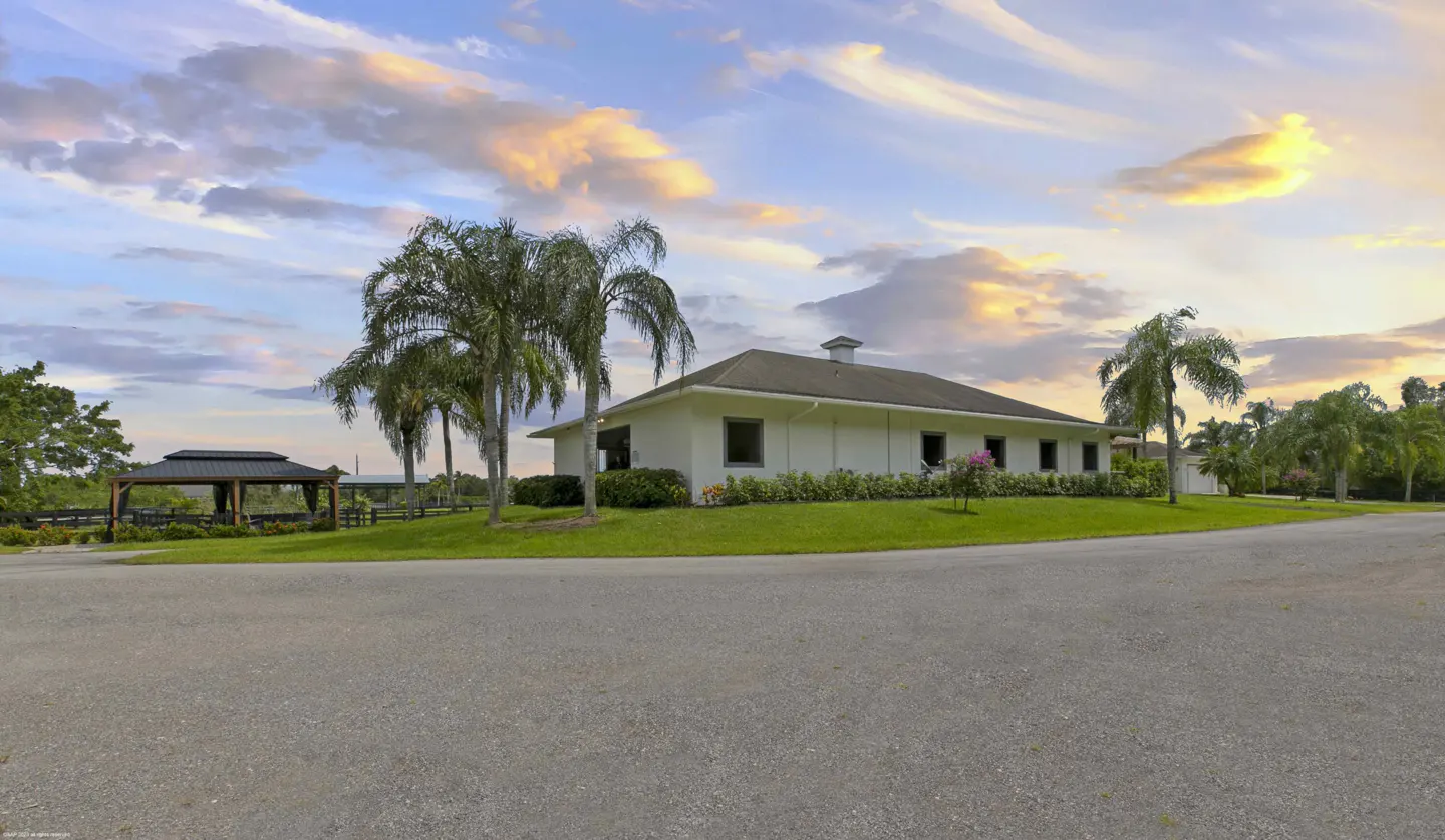 A white ranch-style house with palm trees and a gazebo under a blue and orange sky.