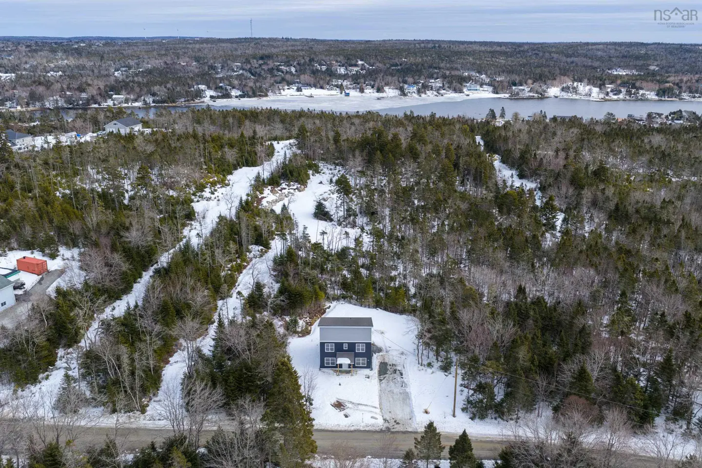 Aerial view of a dark blue house with a gray roof surrounded by snow-covered trees and a lake in the background.