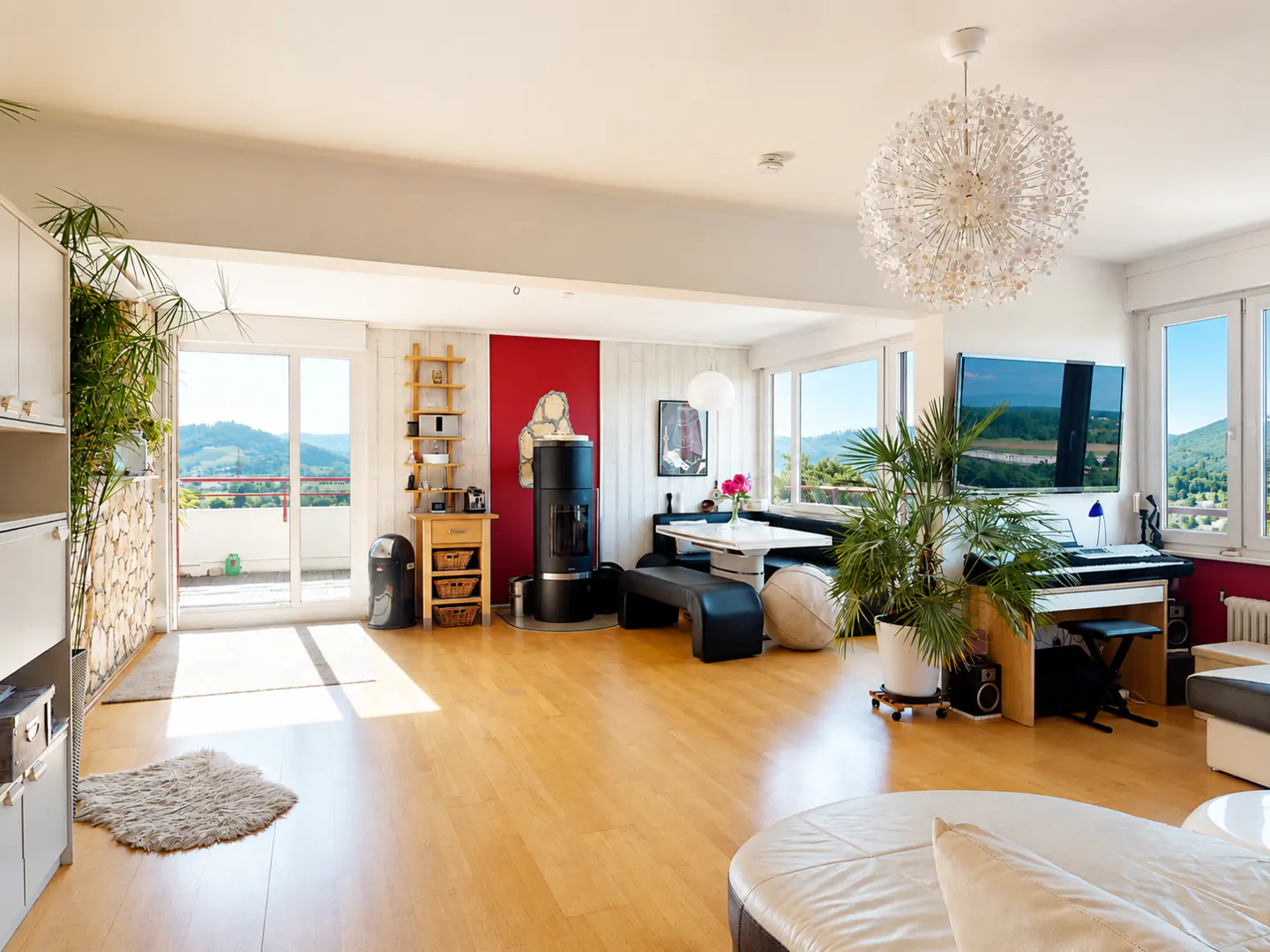 Bright, open-plan living room with light wood floors, a modern fireplace, dining area, and large windows with scenic views.