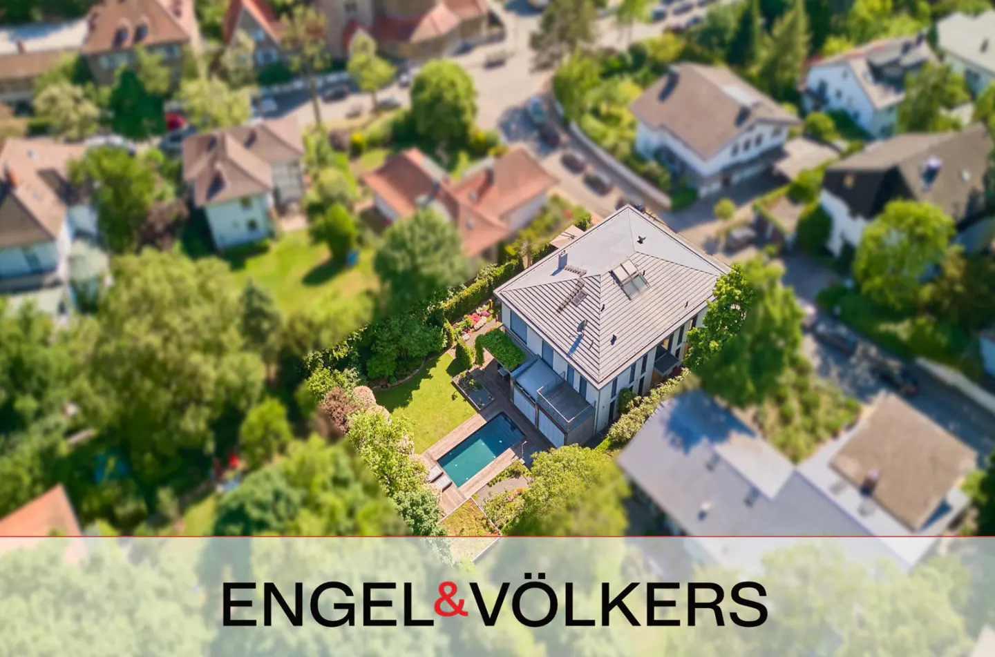 Aerial view of a modern house with a swimming pool and lush green garden in a suburban neighborhood, Engel & Völkers logo.