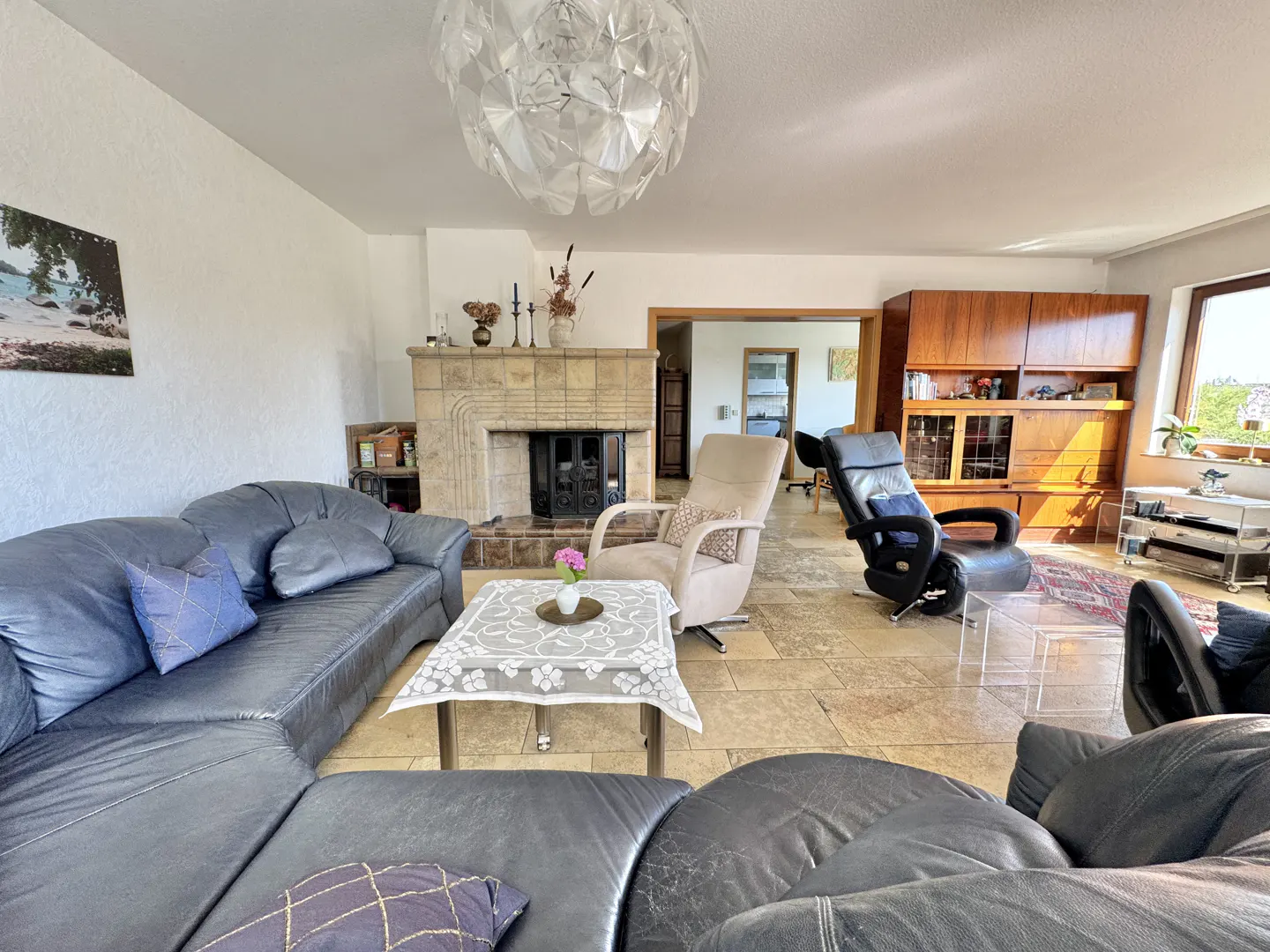 Living room with leather sofas, a stone fireplace, and a large cabinet. A table with a flower sits in the center.