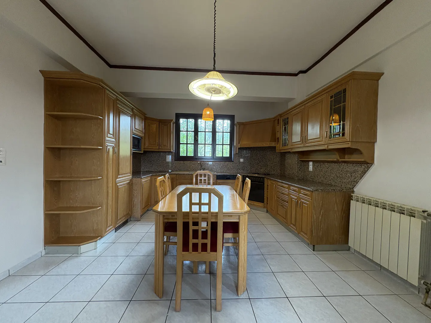 A kitchen with light wood cabinets, a table with red chairs, and a white tile floor.