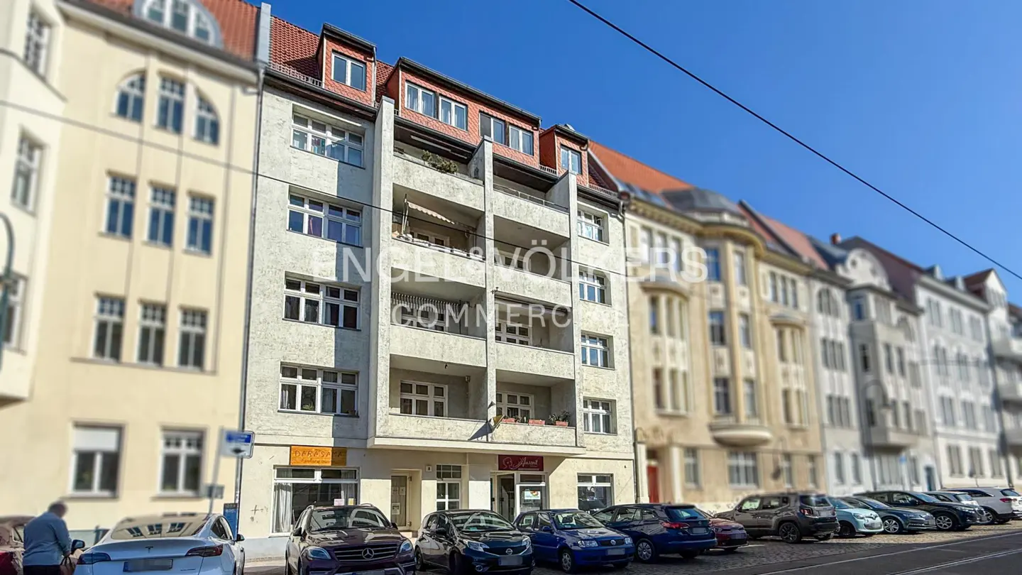 Exterior view of a multi-story building with balconies, street parking, and blue sky.