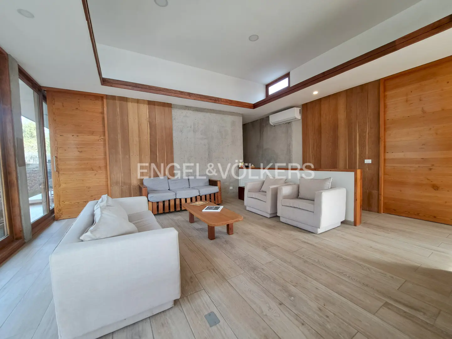 Modern living room with light wood floors, white sofas, a wooden coffee table, and walls featuring wood panels and concrete.