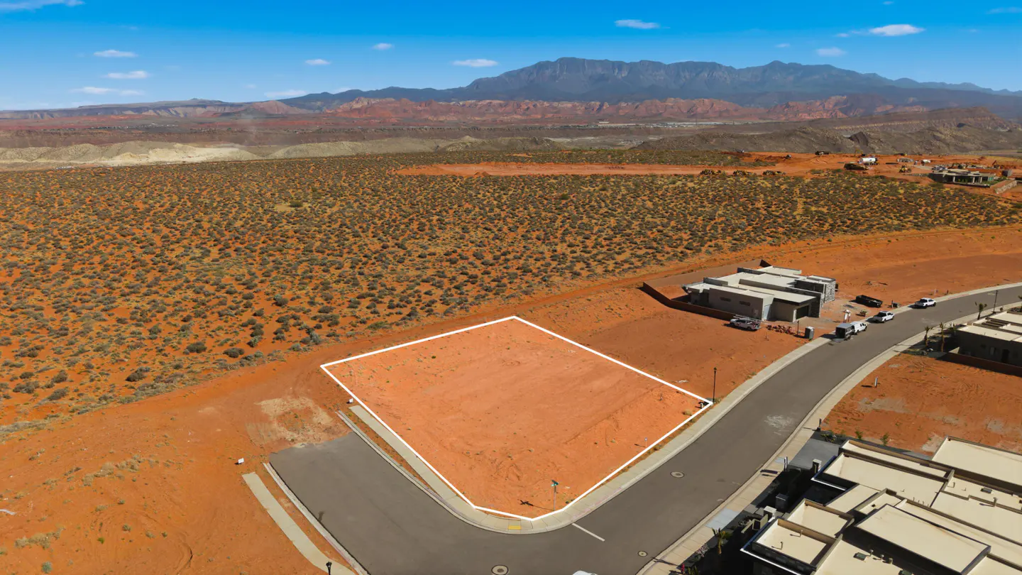 Aerial view of a vacant lot outlined in white, surrounded by desert landscape and mountains under a blue sky.