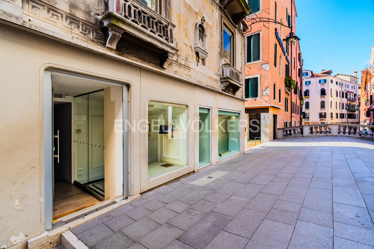 Exterior view of a building with an open door and display windows on a stone-paved street in Venice, Italy.