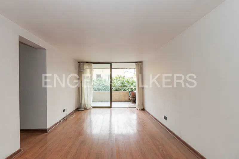 Empty living room with hardwood floors, white walls, and sliding glass doors to a balcony with greenery.