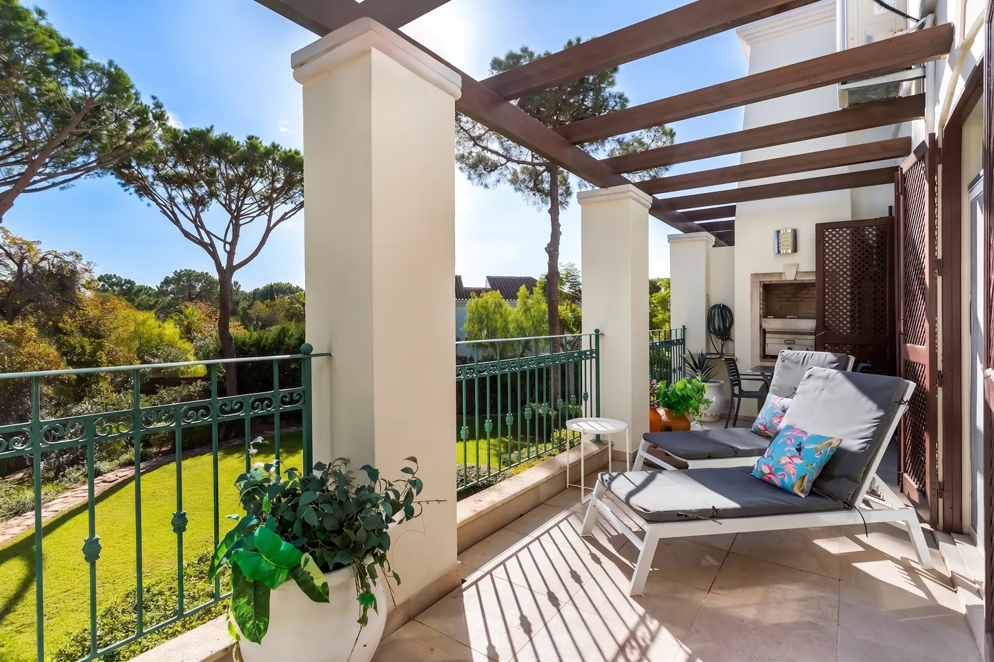 Balcony with two lounge chairs, green iron railing, and a view of a green lawn and trees under a blue sky.