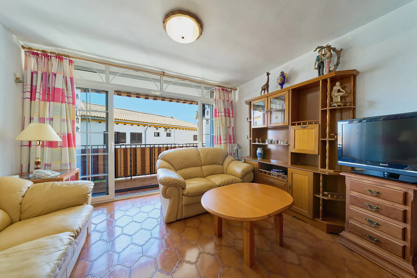 Living room with two beige leather sofas, a round wooden coffee table, a large wall unit, and a balcony with a view.