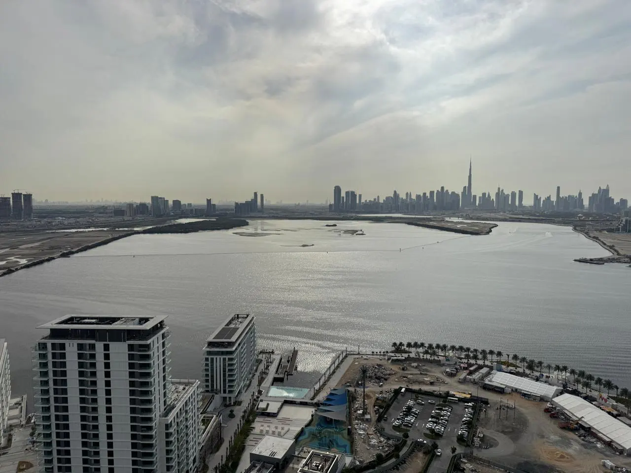 Dubai skyline view from a high-rise apartment, featuring the Burj Khalifa, a body of water, and construction sites.
