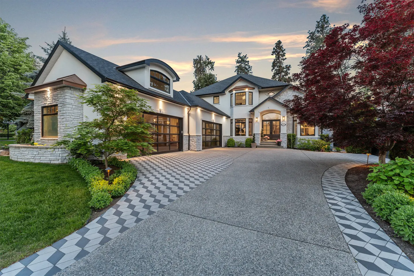 Exterior view of a two-story white house with a black roof, stone accents, and a patterned driveway.