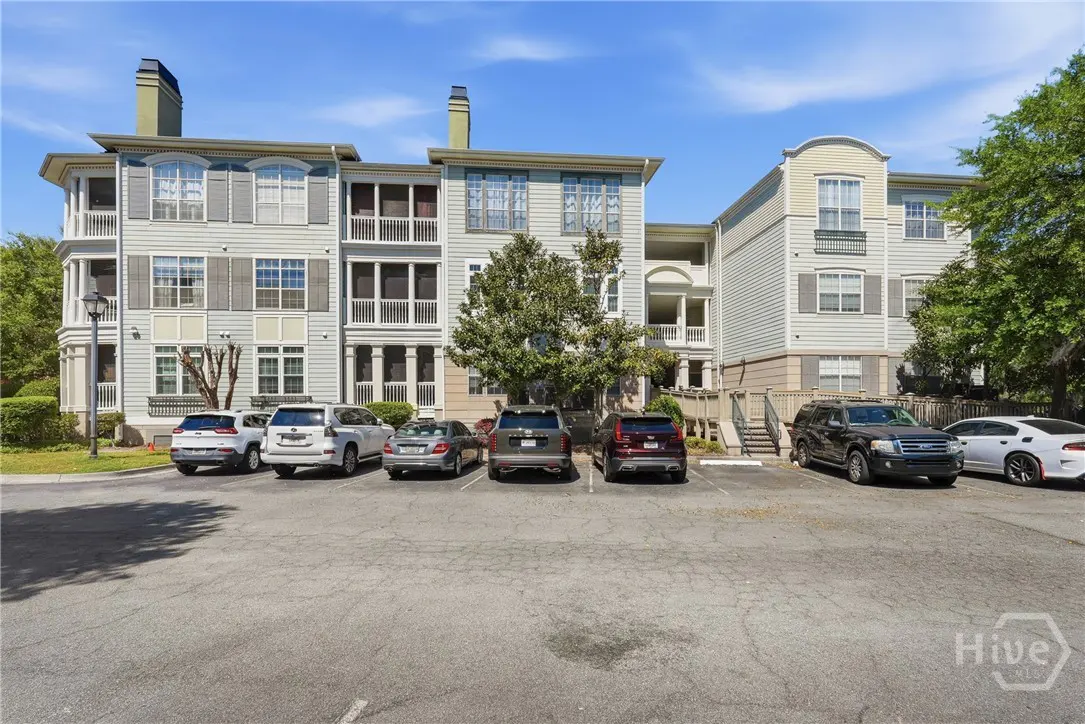 Exterior view of a three-story apartment building with gray siding and gray shutters, with cars parked in front.