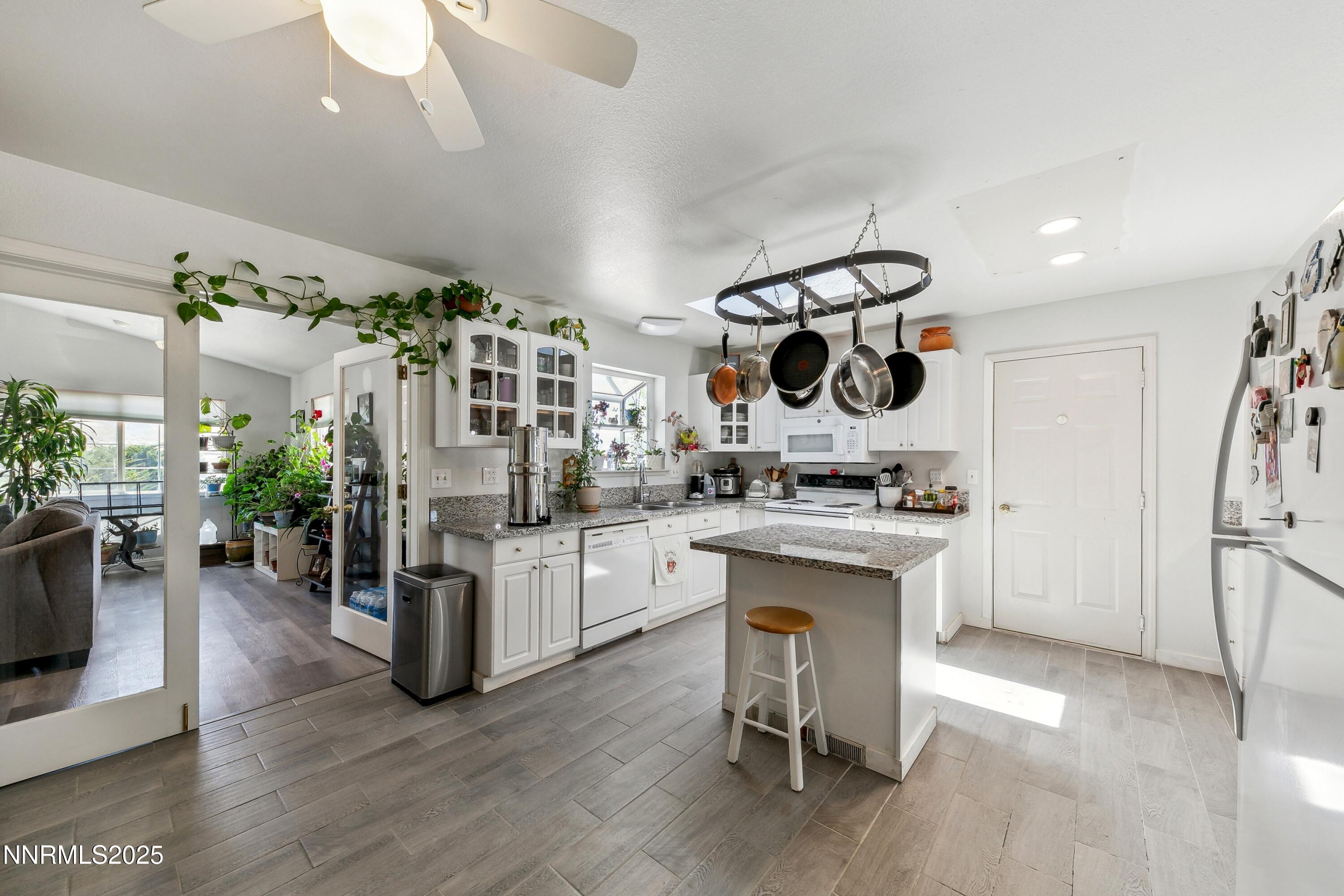 Bright kitchen with white cabinets, granite countertops, a central island with a stool, and a hanging pot rack. [AI-generated text]