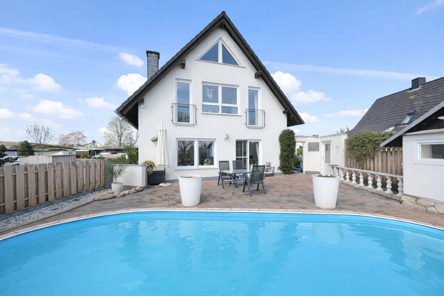 A white two-story house with a black roof and a blue swimming pool in the foreground.