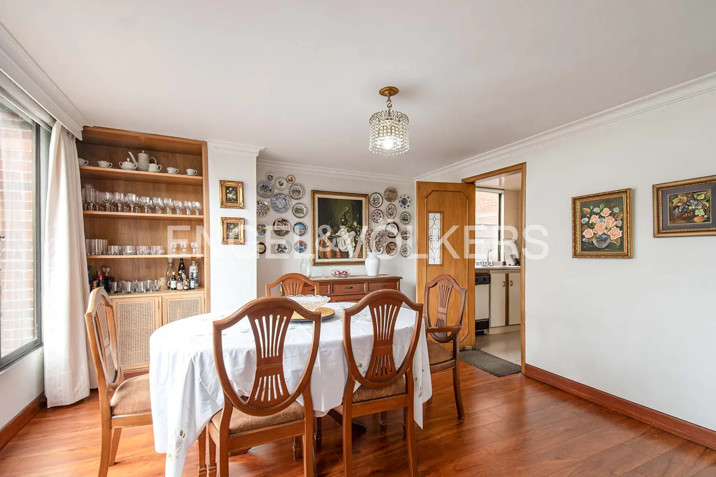 A dining room with a wood table, chairs, and hardwood floors. A china cabinet and decorative plates adorn the walls.