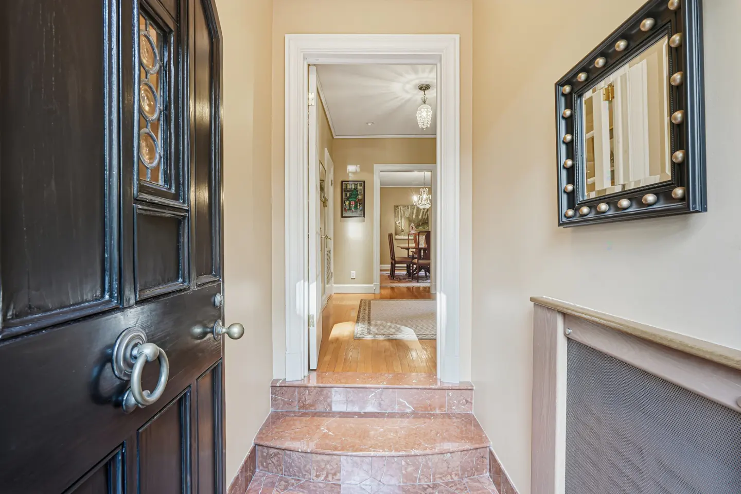 A foyer with marble steps leads to a hallway with hardwood floors and a dining room. A black door is on the left.