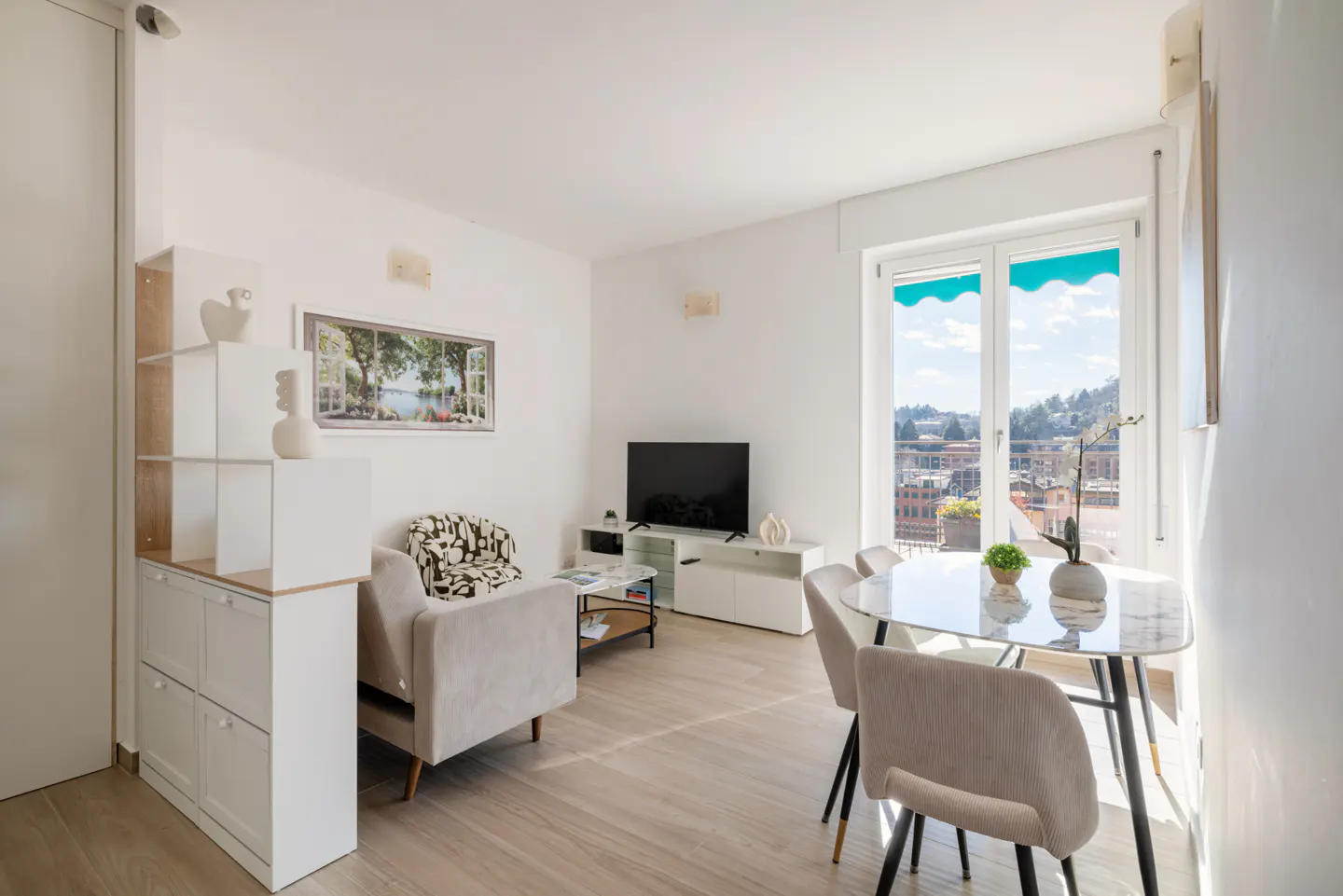 Bright living room with a glass table, four chairs, a sofa, and a large window with a city view.