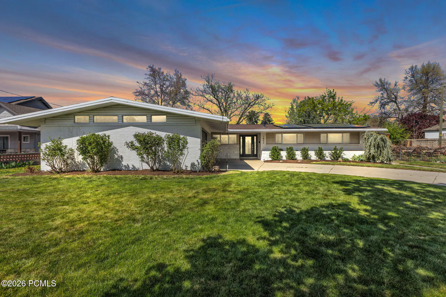 A single-story home with a green lawn and a colorful sunset sky.