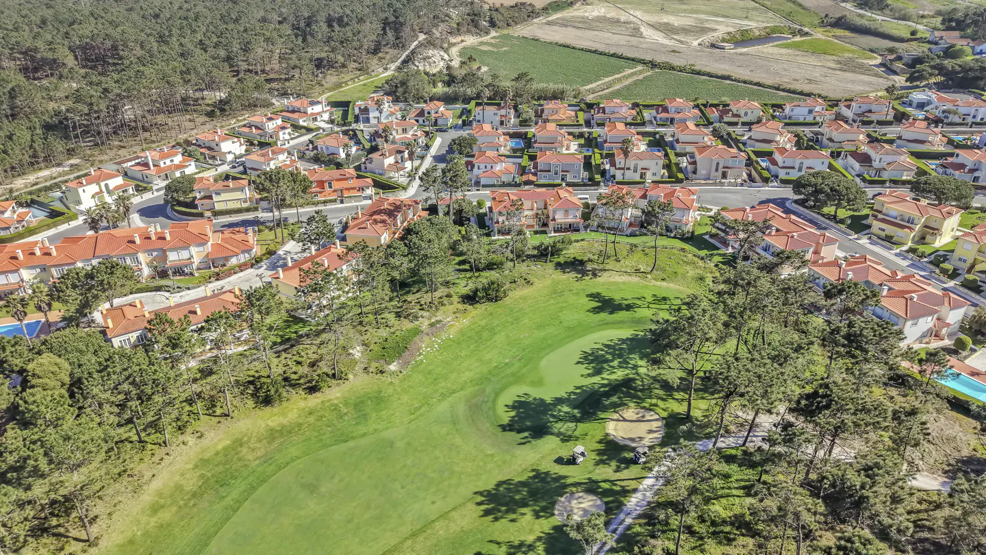 Aerial view of a residential area with red-roofed houses bordering a green golf course with trees.