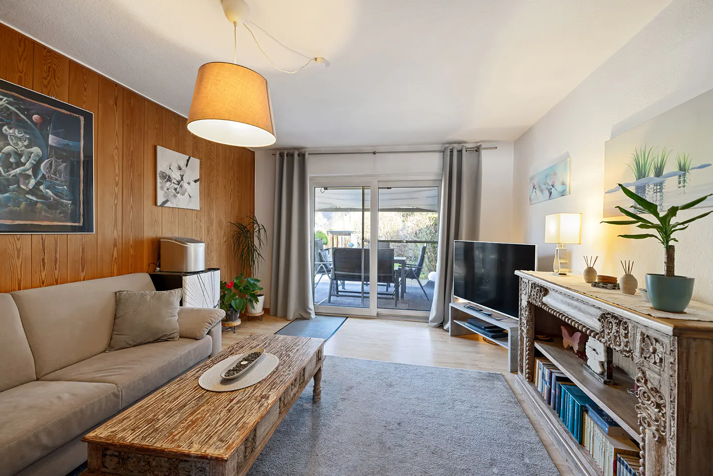 Living room with wood paneled wall, beige sofa, rustic coffee table, and sliding glass doors to a patio.