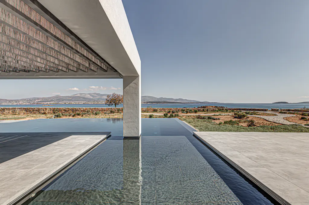 Modern villa with a pool overlooking the ocean. White pergola with reed roof. Blue sky and water.