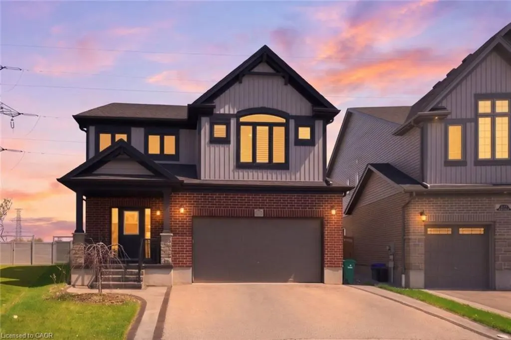 Two-story house with gray siding, brick base, and a two-car garage under a colorful sunset sky.